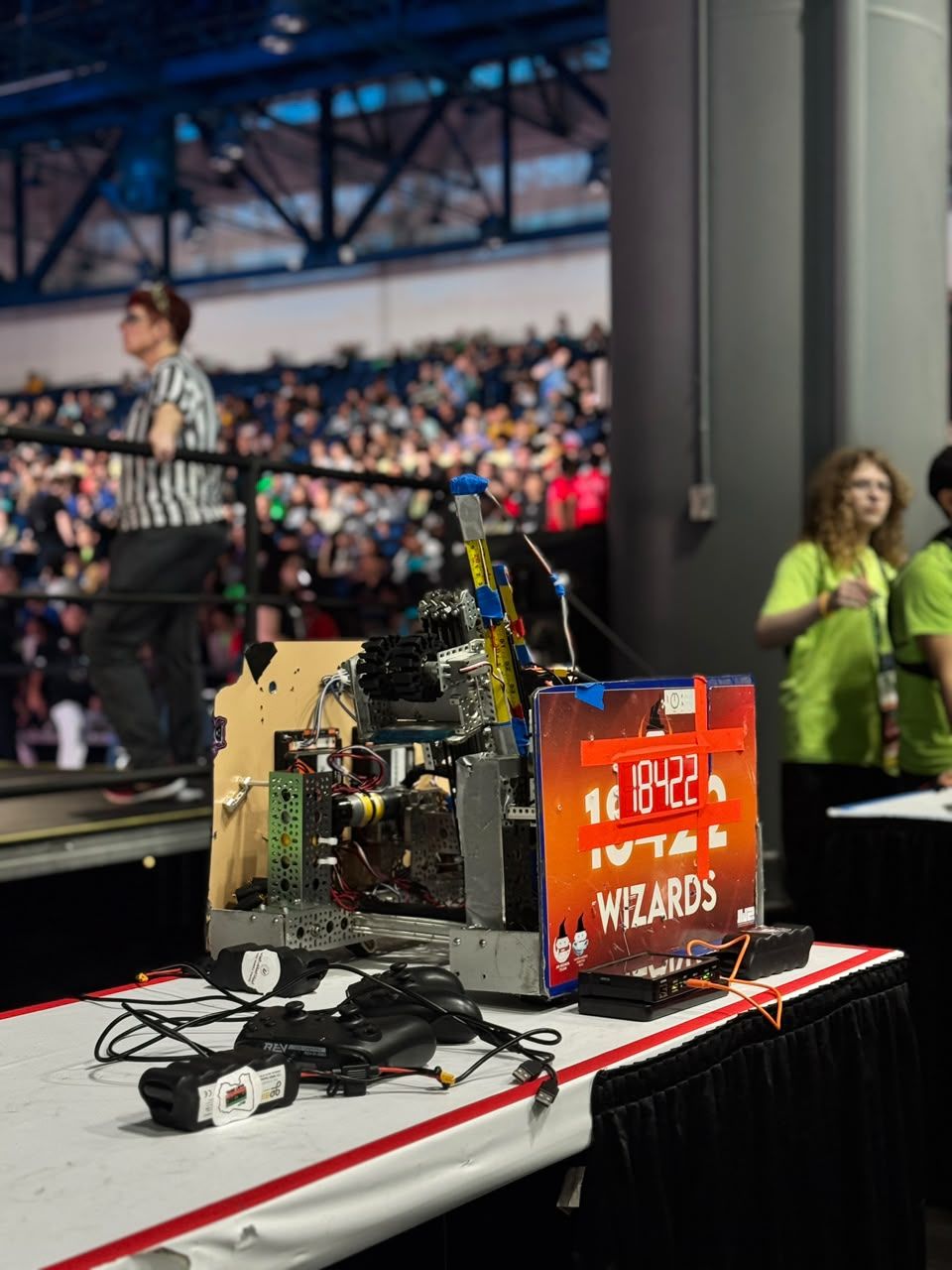 The team’s competition robot on a field-side table, its number plate reading 18422 Wizards, with a packed arena behind it.